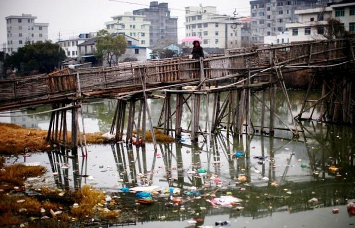 Женщина переходит по мосту реку, несущую тонны мусора, Вэньчжоу.